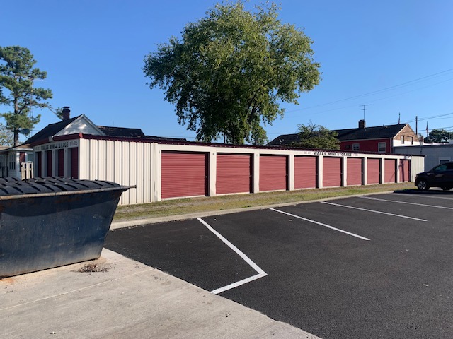 Row of red roll-up storage unit doors beside a paved parking lot