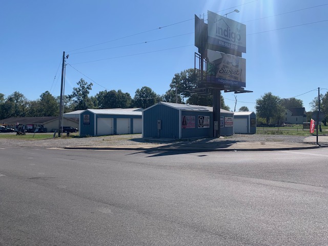 Blue storage buildings with white roll-up doors along the road